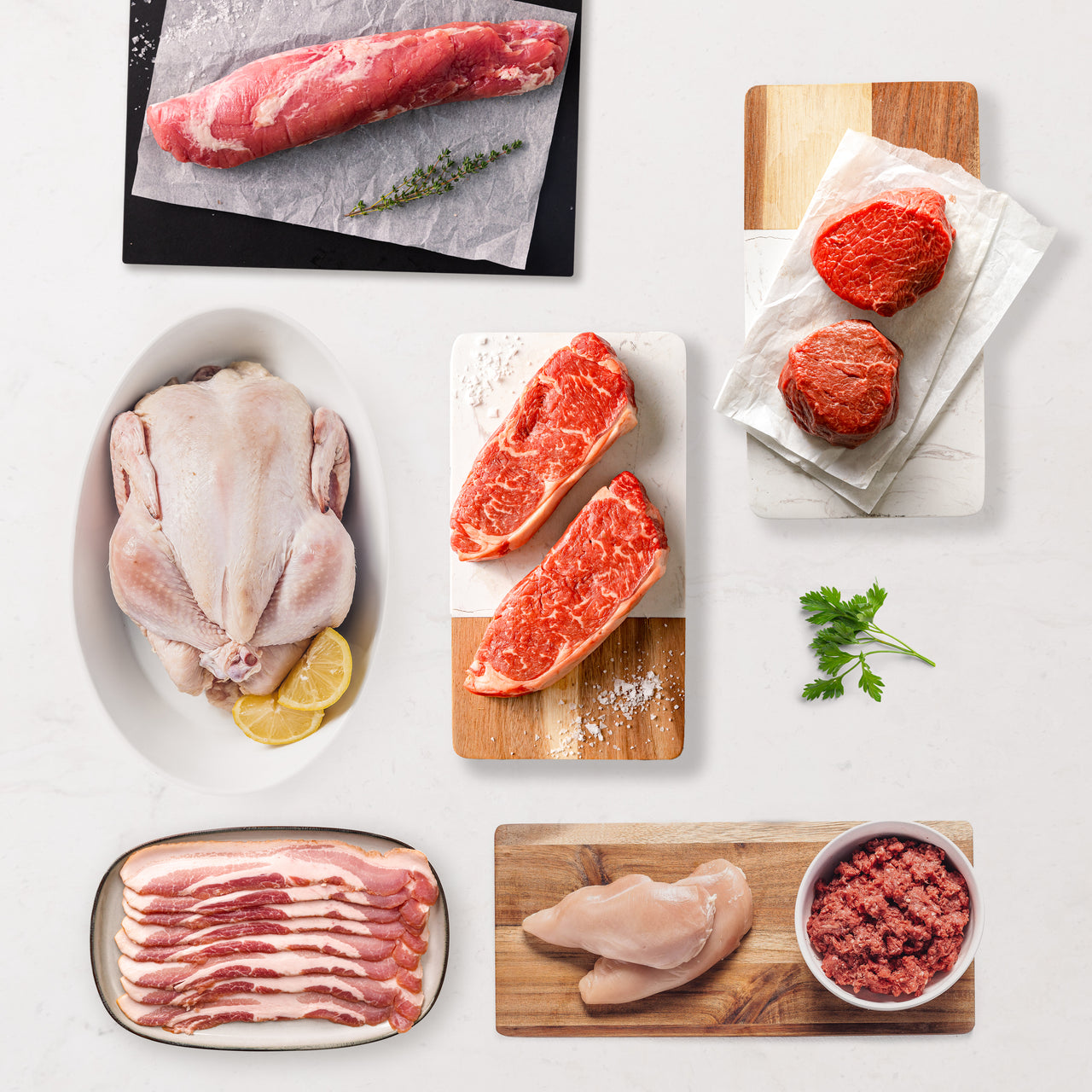 Assorted raw meats including steak, chicken, and ground meat on a white surface with wooden cutting boards.